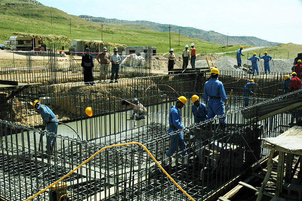 Workers in hardhats pouring cement into steel foundation